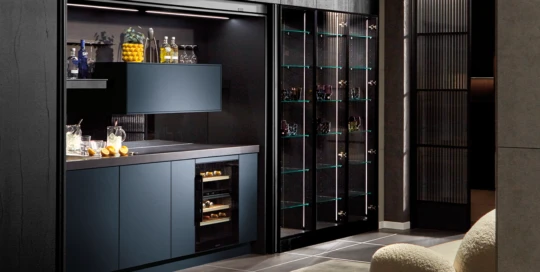Eine moderne pronorm Designküche als Bar, dunklen Fronten und eleganter Glasvitrine im offenen Wohnraum.