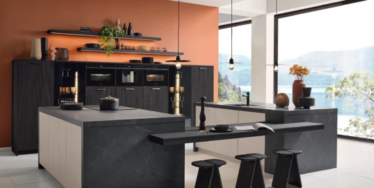 Elegant kitchen interior by pronorm featuring island with seating, built-in appliances and panoramic lake view.