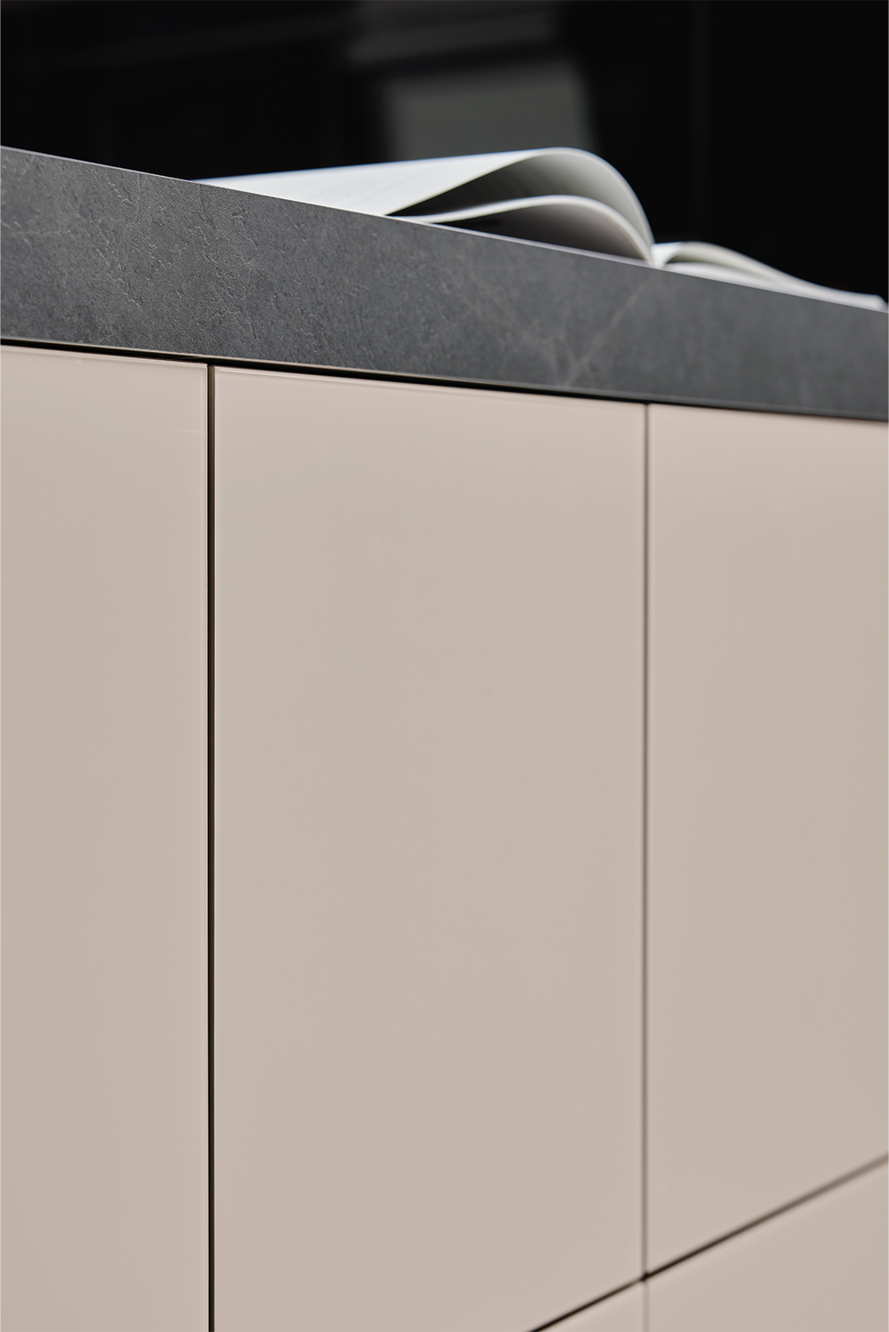 Detailansicht einer pronorm-Küchenfront in Beige mit dunkler Stein-Arbeitsplatte – klare Linien und edle Haptik.