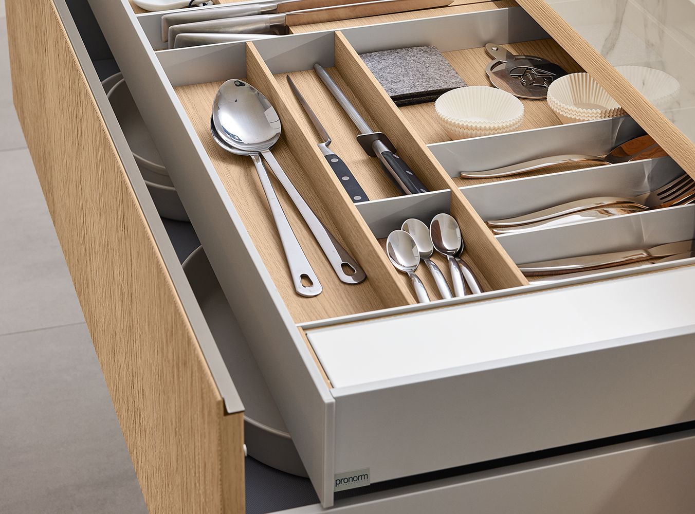 Offener pronorm Schubkasten mit durchdachter Innenausstattung für Besteck und Küchenhelfer – edler Holz-Look kombiniert mit funktionalem Design.