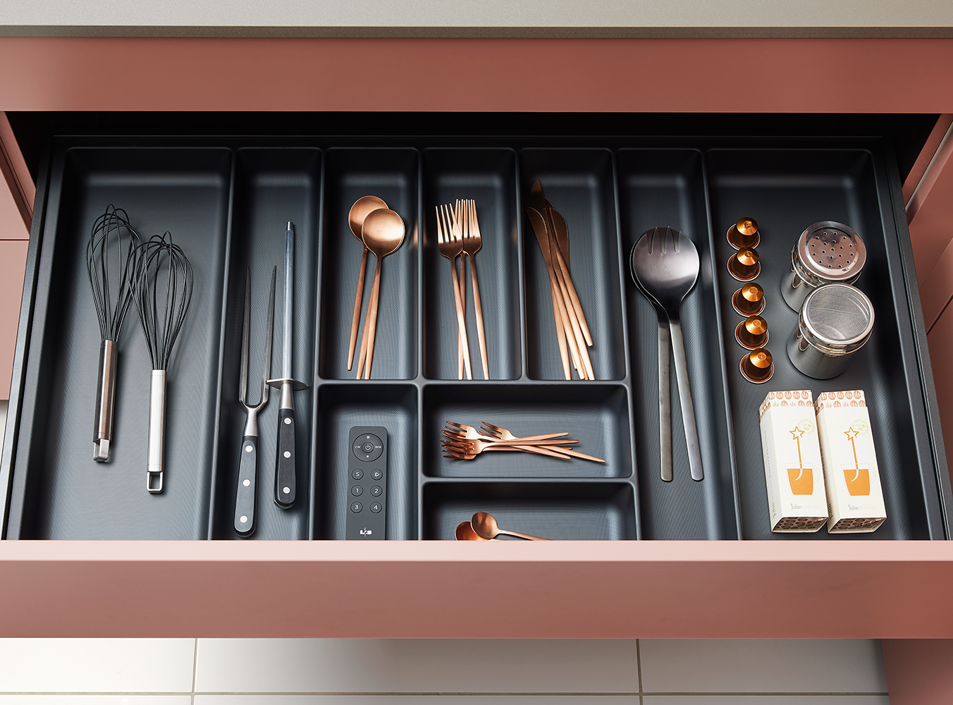 Interior of a pronorm drawer in dark grey with organized cutlery insert and modern copper-toned utensils – elegant and functional kitchen storage.