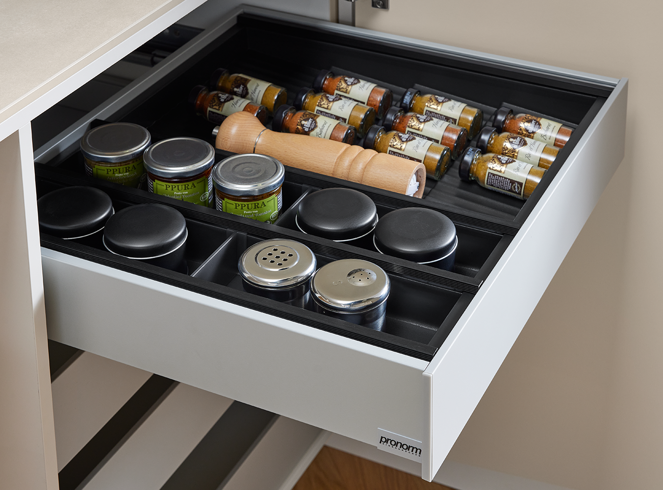 Interior of a pronorm drawer with premium spice jar insert, storage containers and pepper mill – smart and elegant kitchen organization.