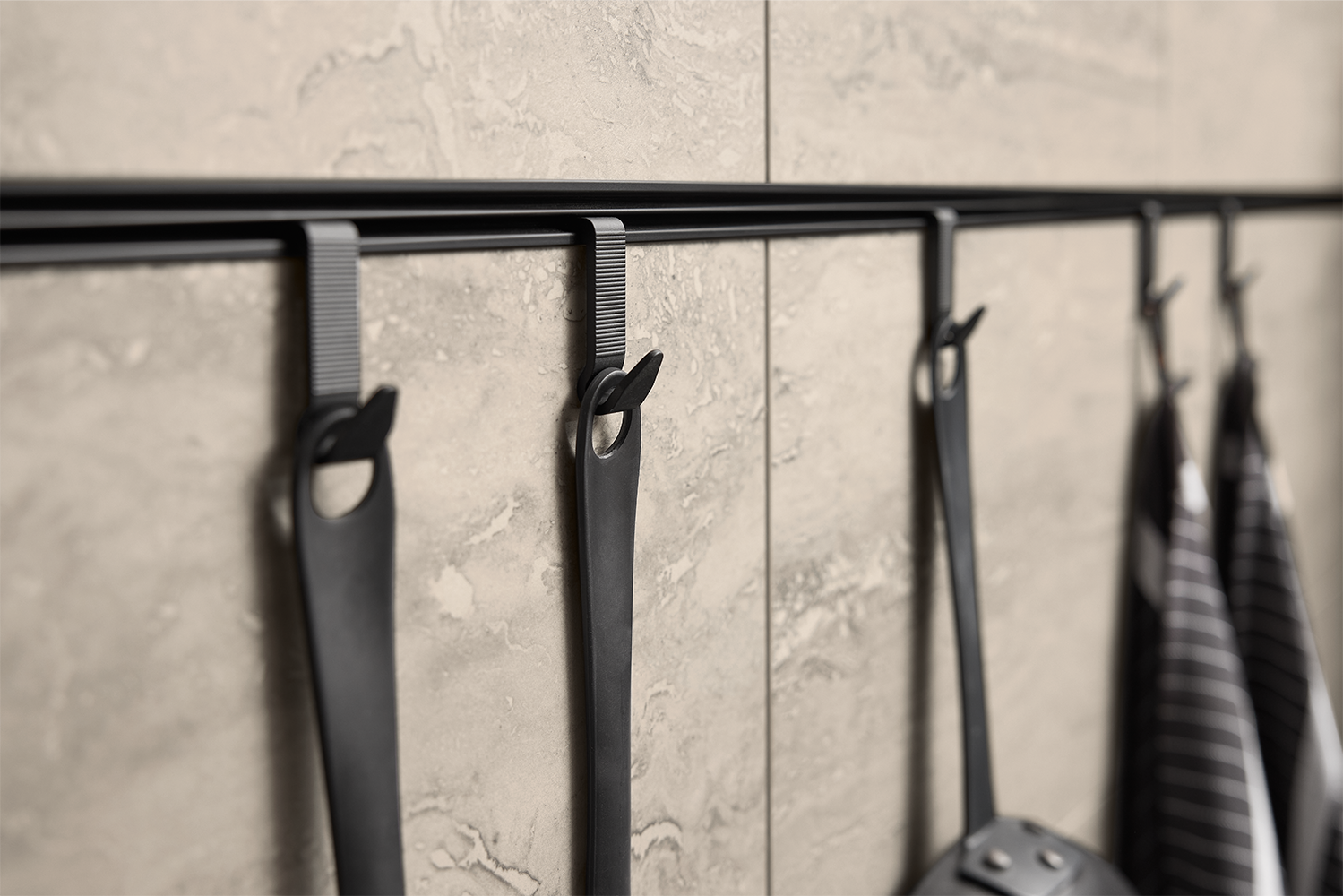 Black wall hooks mounted on stone-look panel, part of walnut and stone handleless kitchen by pronorm