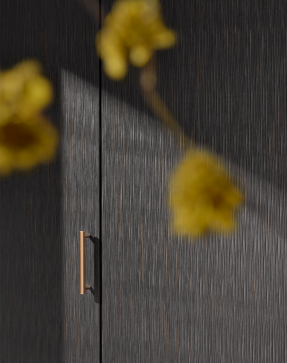 Detailaufnahme einer strukturierten pronorm Küchenfront mit goldfarbenem Griff im Spiel von Licht und Schatten – akzentuiert durch florales Dekor.