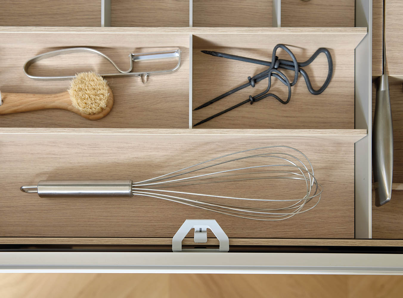 Vue détaillée de l’intérieur du tiroir pronorm avec organiseur en aspect bois, contenant fouet, brosse de cuisine et ustensiles – pratique et raffiné.
