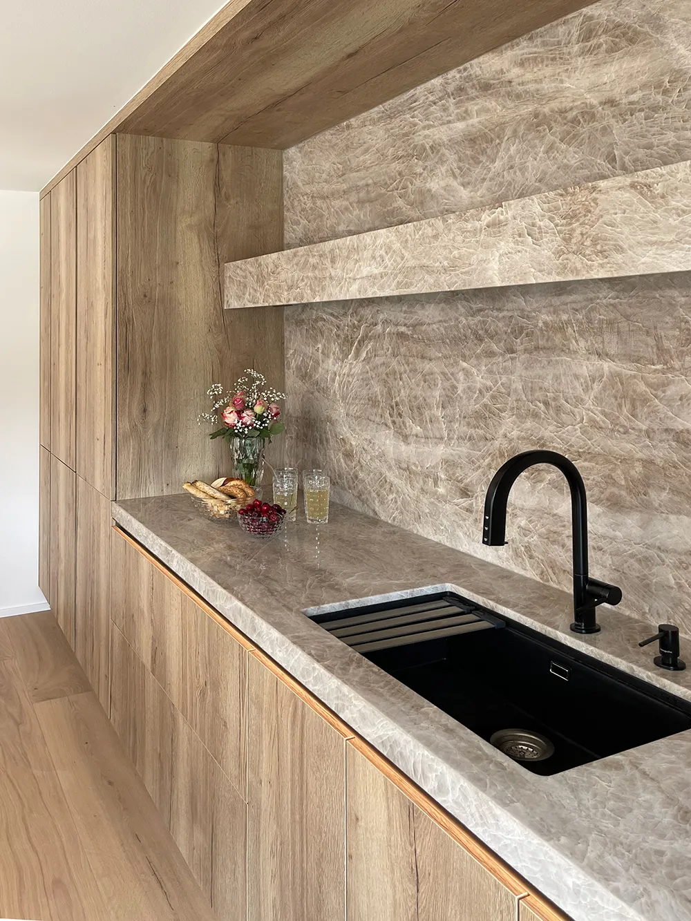 Detail einer pronorm Küche mit Arbeitsplatte und Rückwand in Taj Mahal Optik, Eichenfronten und schwarzer Spüle