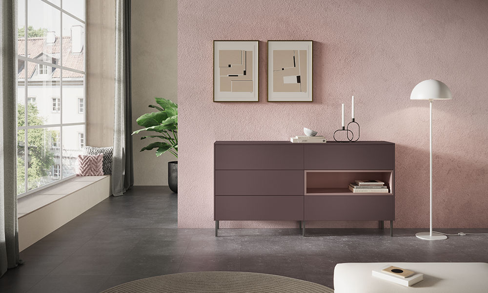 Modernes Sideboard in Velvet-Mattlack mit offenen Fächern und schwarzen Metallfüßen in einem hellen, eleganten Wohnraum mit rosafarbener Wand und großer Fensterfront – pronorm Designmöbel.