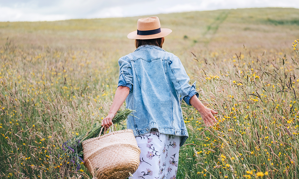 Frau mit Strohhut und Korb in einer blühenden Sommerwiese – symbolisches Bild für nachhaltige Materialien, umweltbewusste Produktion und ressourcenschonende Küchenfertigung bei pronorm.