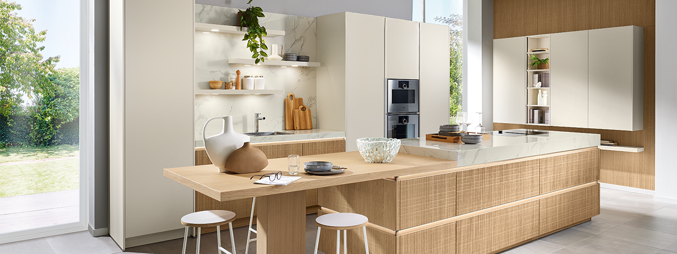 Une cuisine pronorm de style bohème avec une façade en placage particulière et une grande île avec table attenante.