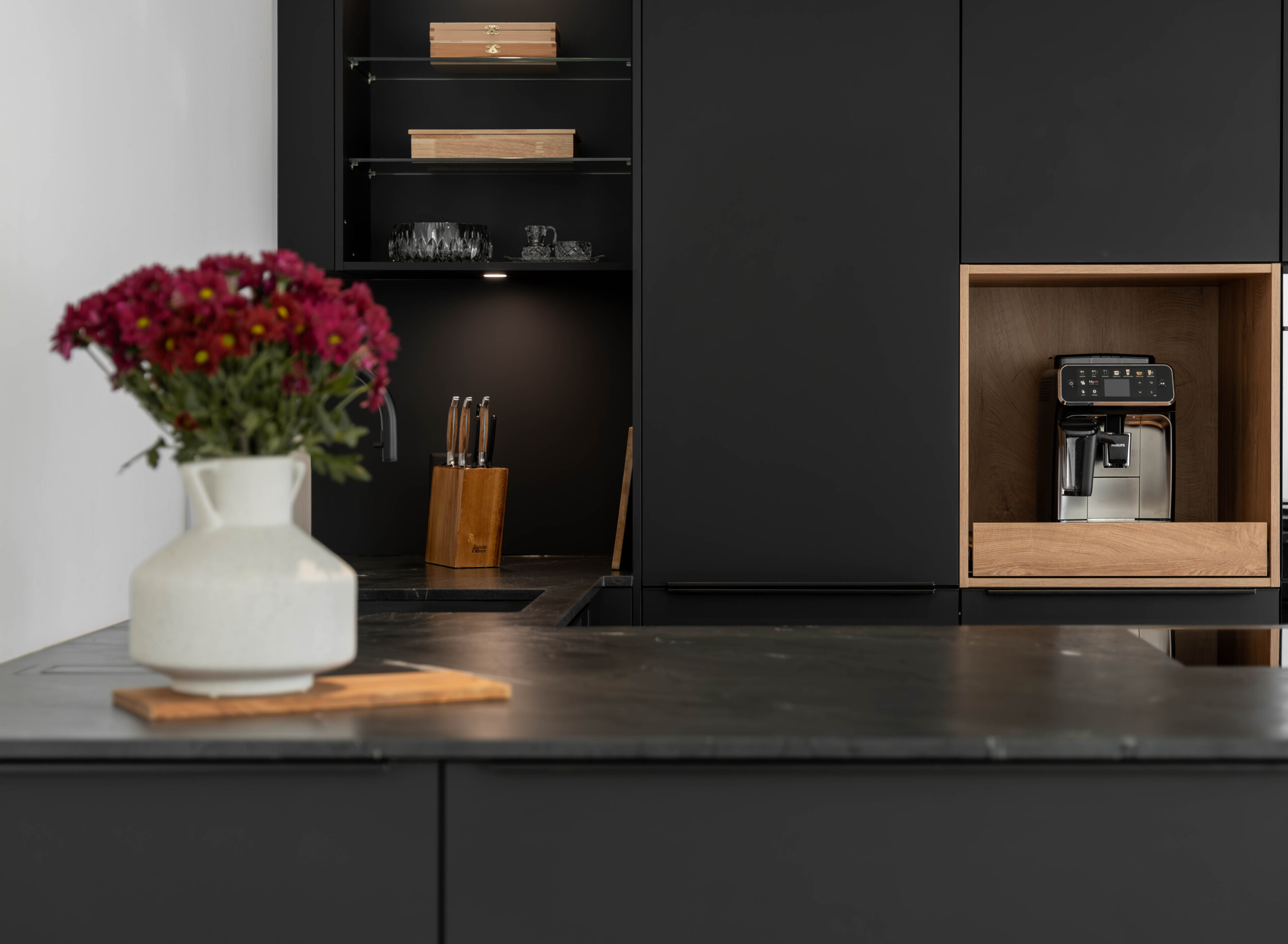 Elegante Einbauküche in Schwarz mit warmen Holzfronten und moderner Kochinsel – hochwertige Materialien für zeitloses Küchendesign.