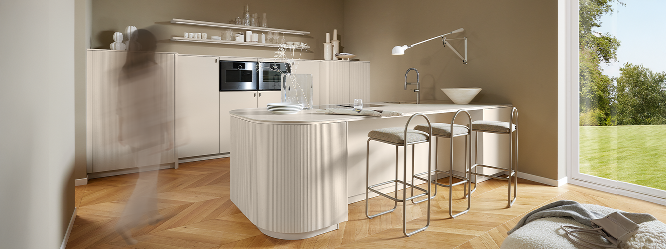 A light pronorm kitchen with a rounded island and fronts in the colour of the year 2026.