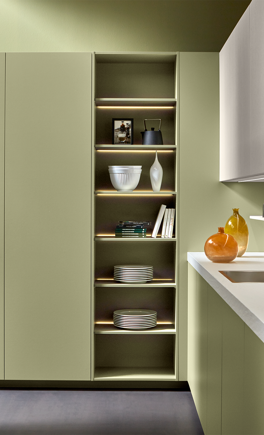 cuisine pronorm en vert et blanc avec une armoire haute dotée d’une niche ouverte éclairée.