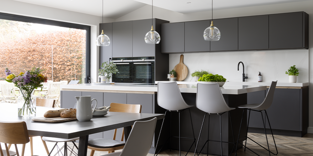 A dark grey, modern and high-quality kitchen by pronorm with a kitchen island and bar area.
