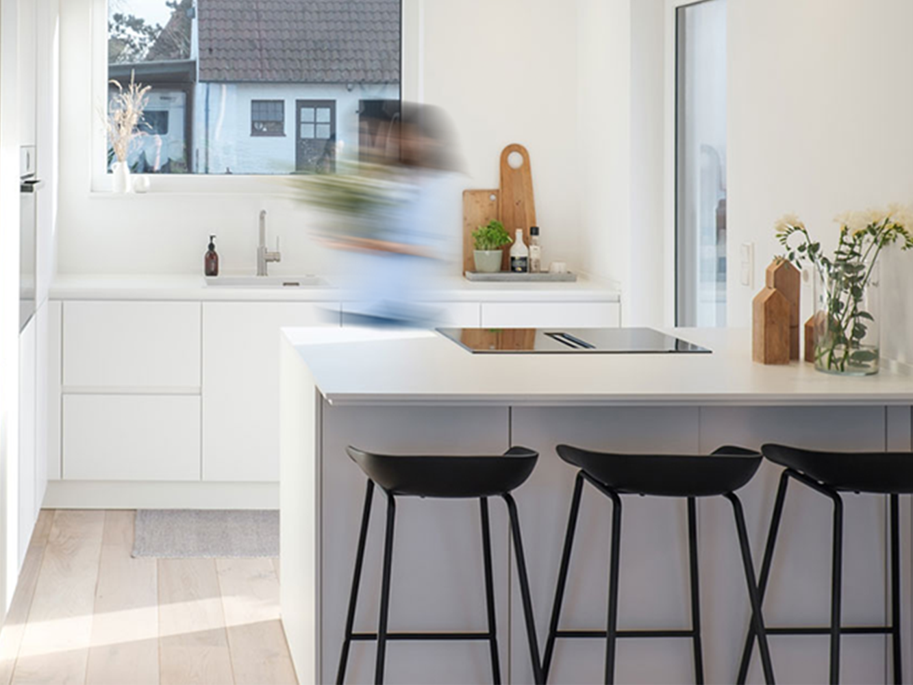 A bright, white modern handleless pronorm kitchen with tall units and a kitchen island with bar stools.