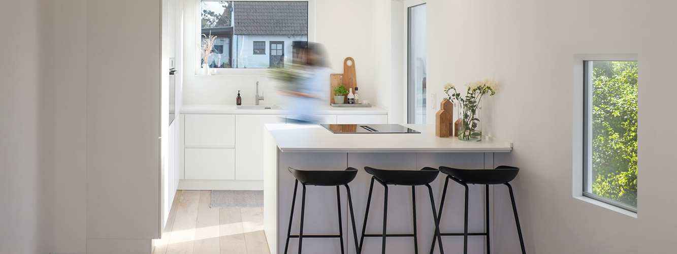 A modern white handleless pronorm kitchen with an island and bar stools.